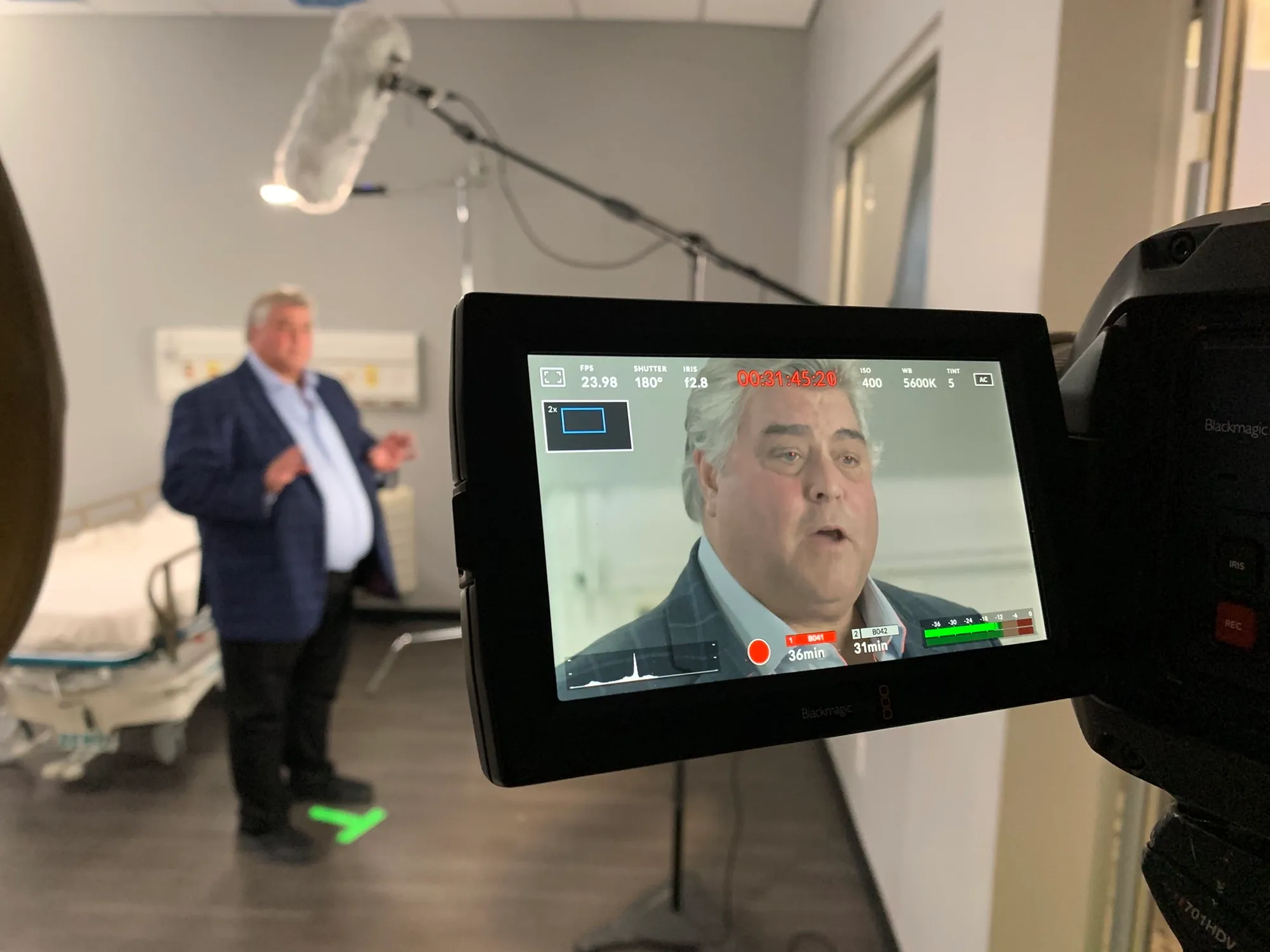 Filming a speaker in a mock hospital room; a camera monitor in the foreground frames his interview portrait.